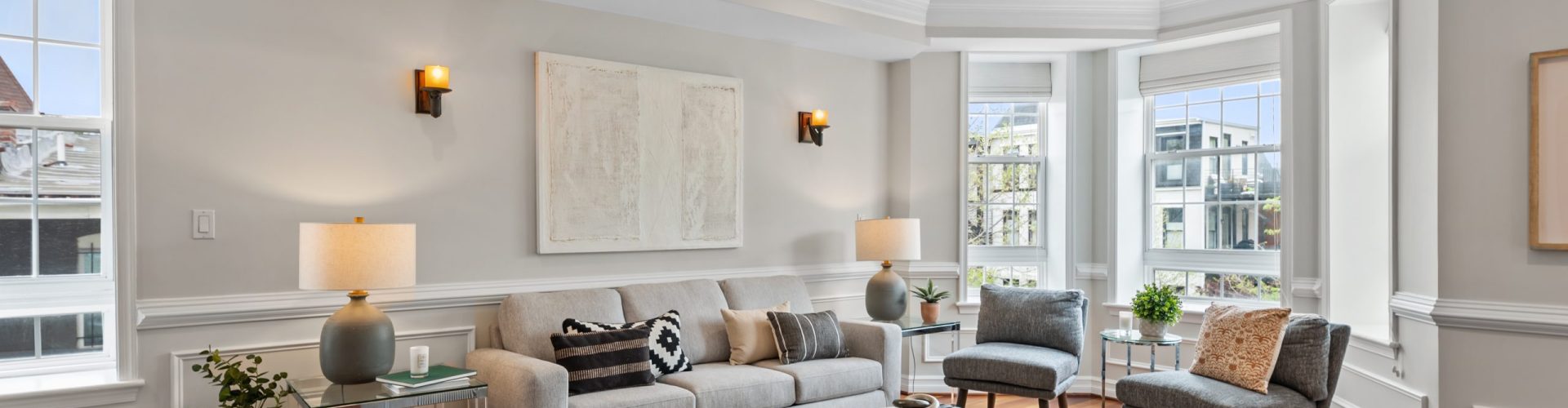 Gallery Image – Refined Living Room with Bay Windows | Prismatic Home Photography Bright living room with crown molding, bay windows, neutral furniture, hardwood floors, and natural light accentuating modern decor.